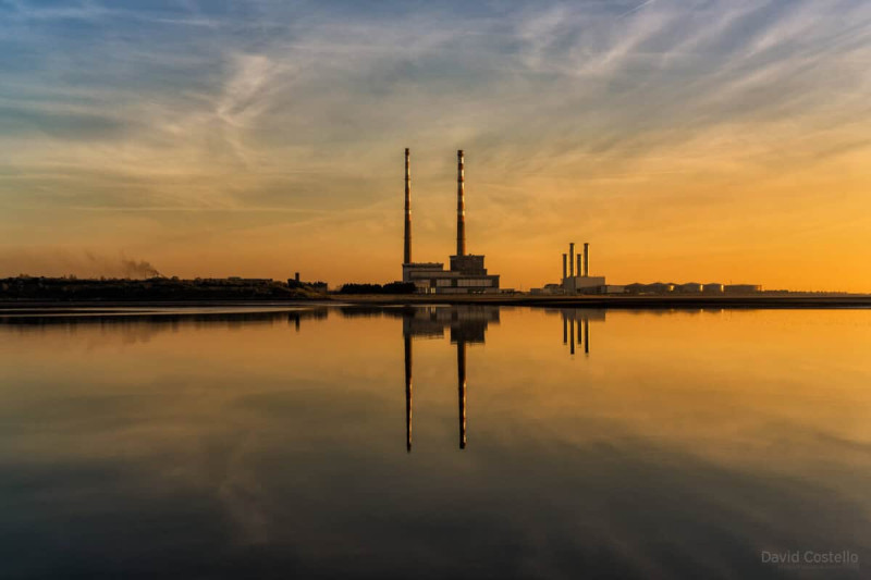 zicht op twee industriële schoorstenen, rood-wit gestreept bij zonsopkomst, in havenlandschap